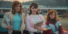 three women standing next to each other in front of a car holding papers and folders