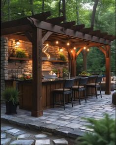 an outdoor kitchen and bar area with lights on the roof, surrounded by stone pavers