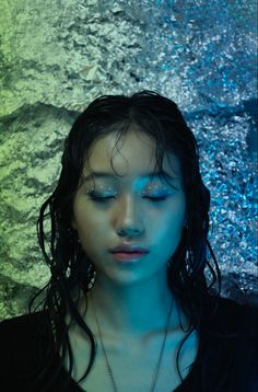 a woman with long hair and blue makeup is standing in front of an abstract background