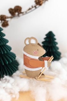 a paper cut out of a mouse on a sled in front of christmas trees