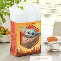 a star wars baby yoda bag sitting on top of a table next to a cup of coffee