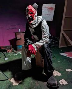 a man with red paint on his face and hands sitting in front of a box