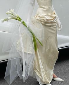 a woman in a wedding dress holding a bouquet of tulips next to a white car