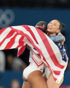 two female athletes hugging each other with an american flag draped over them in the background