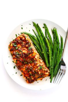 a white plate topped with fish and green beans next to a fork on top of a table