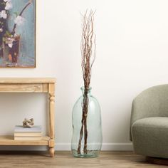 there is a vase with branches in it next to a chair and a painting on the wall