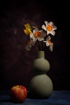 a green vase with flowers and an apple