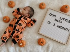 a baby laying next to a sign that says our little boo is 1 month