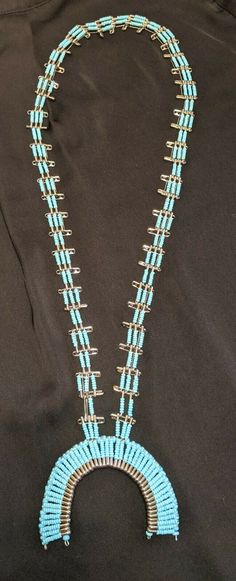 a necklace with blue beads and silver accents on a black cloth covered background, in the shape of an arch