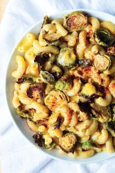 a white bowl filled with pasta and brussels sprouts on top of a table