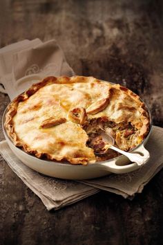 a pie sitting on top of a wooden table next to a piece of paper with a fork in it