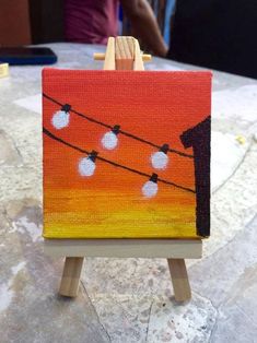 an easel with a painting on it that has lights strung in the sky above