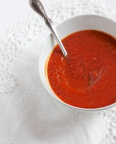 a white bowl filled with red sauce on top of a doily next to a spoon