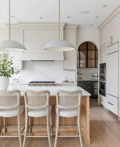 a kitchen with white cabinets and marble counter tops, three pendant lights over the island