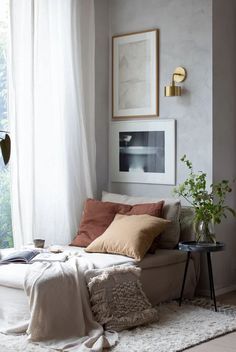 a white couch sitting under a window in a living room next to a table with plants