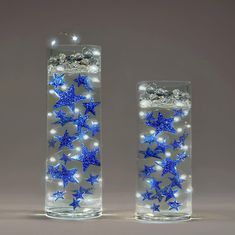 two clear vases with blue stars in them on a gray background, one is lit up and the other has white lights