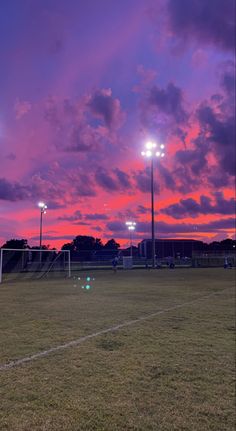 a soccer field at sunset with the sun setting in the distance and people playing on it