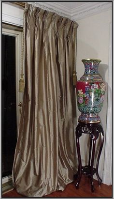 a vase sitting on top of a table next to a window covered by a curtain