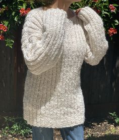 a woman wearing a white sweater and jeans standing in front of a flowered fence