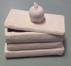 a stack of three white ceramic books with an apple sitting on top of one book