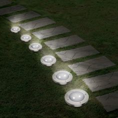 several white lights are placed on the grass in front of some stepping stones and concrete steps