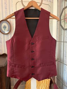 This handsome vest is burgundy with a black sheen/shift on one side and solid black on the other side! It has the original buttons, with three outer pockets on the burgundy side (two of them haven't been opened/unstitched yet) and one chest pocket on the black side. The measurements, taken with the vest lying flat, are: shoulder to shoulder, 12 inches; armpit to armpit, 19 inches; length, 25 1/2 inches in front and 22 inches in back; bottom edge, 17 1/2 inches. In very good condition. Burgundy Vest Outfit Men, Maroon Vest Outfit Men, Classic Fitted Winter Vest, Classic Fitted Vest For Winter, Formal Winter Vest With Pockets, Tailored Sleeveless Vest Outerwear, Formal Black Vest With Pockets, Sleeveless Business Vest Outerwear, Formal Sleeveless Fall Vest