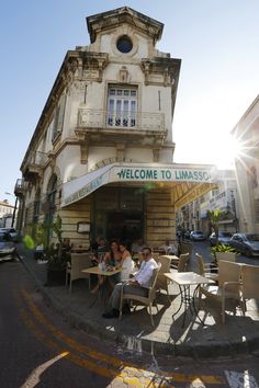 people sitting at tables in front of a building with a welcome to limasso sign