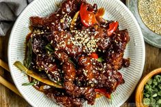 a white plate topped with meat covered in sauce and sesame seeds next to a bowl of green beans