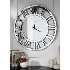 a large white clock hanging on the wall above a table with flowers and vases