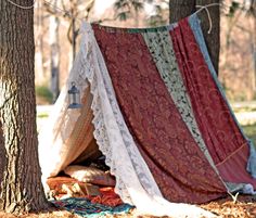 a tent is set up in the woods with blankets and rugs on the ground