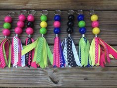 several different colored tassels are lined up on a wooden table with beads and keychains