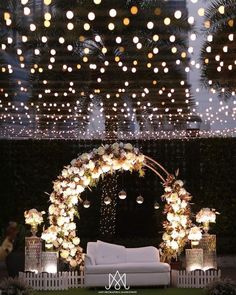 an outdoor wedding setup with white couches and lights hanging from the ceiling above it