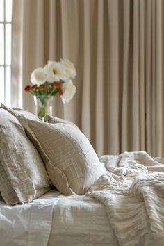 a vase with flowers in it sitting on top of a bed next to two pillows