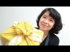 a woman holding a yellow gift bag with a bow on it's head and smiling at the camera