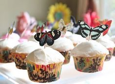 several cupcakes with butterflies on them sitting on a tray in front of other cupcakes