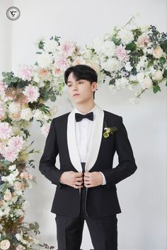 a man in a tuxedo and bow tie standing next to a floral arch