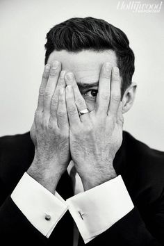 a black and white photo of a man covering his face with his hands while wearing a suit