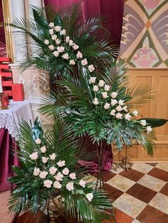 two tall vases with white flowers and greenery in front of a red curtain