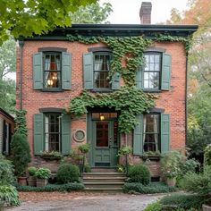 an old brick house with green shutters and ivy growing on the front door, surrounded by greenery