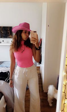 a woman taking a selfie in her bedroom wearing white pants and a pink top