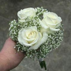 a bouquet of white roses in someone's hand with baby's breath on it