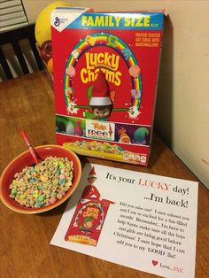 a cereal box with lucky charms next to it and a bowl of cereal on the table