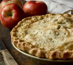 an apple pie sitting on top of a table next to two apples