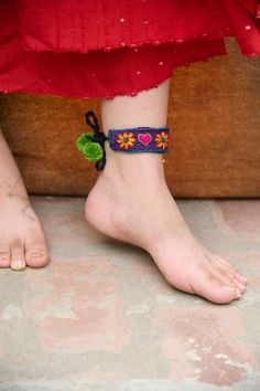 a woman's bare foot wearing a colorful bracelet with flowers and pom poms