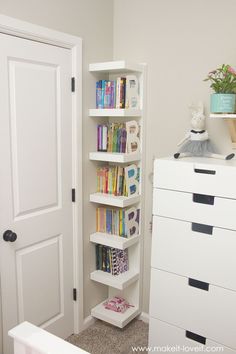 a white book shelf sitting in the corner of a room next to a dresser and door