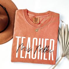 a t - shirt that says teacher next to a hat