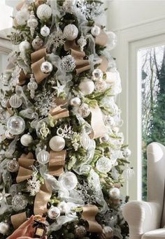 a decorated christmas tree in a living room next to a window with white and gold decorations