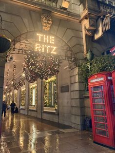 the entrance to an upscale hotel decorated with christmas lights and wreaths, in front of a red phone booth