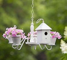 a white birdhouse hanging from a chain with pink flowers