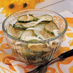 a glass bowl filled with sliced cucumbers on top of a table next to a fork